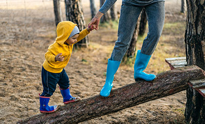 child and adult holding hands while walking on a log