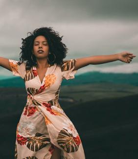 Black women in a white patterned dress with her eyes closed and arms stretched out