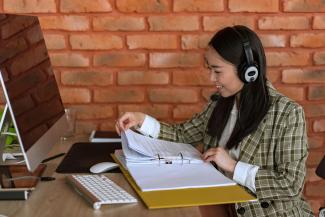 Woman sitting at a desk, wearing headphones and looking at papers in a binder